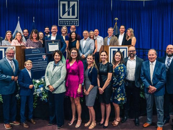 A group of people dressed in formal attire pose together on a stage in front of a Northwood University backdrop, proudly holding certificates and plaques from Northwood's Outstanding Alumni Awards.